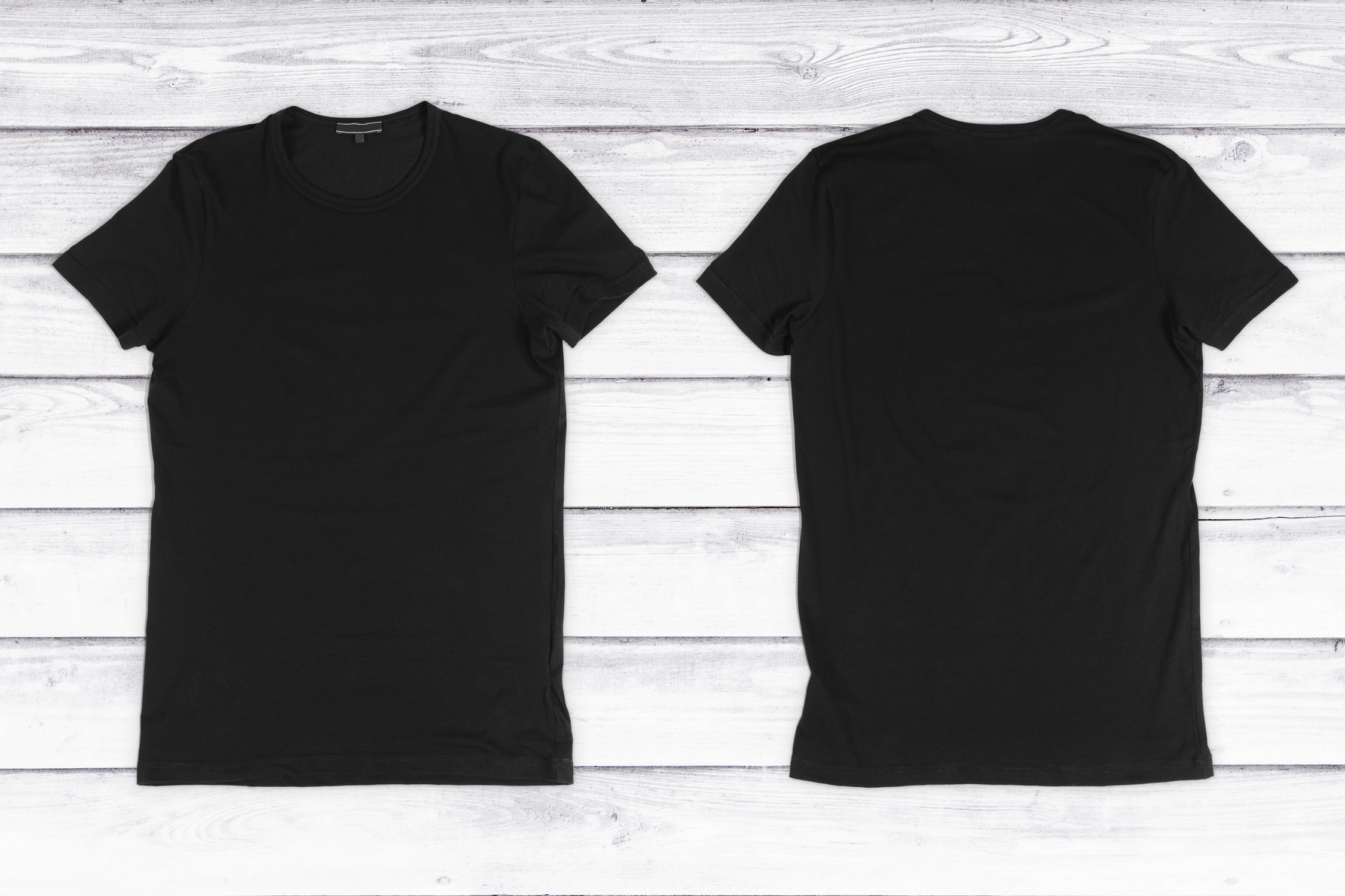 Two black blank T-shirts on a white wooden background